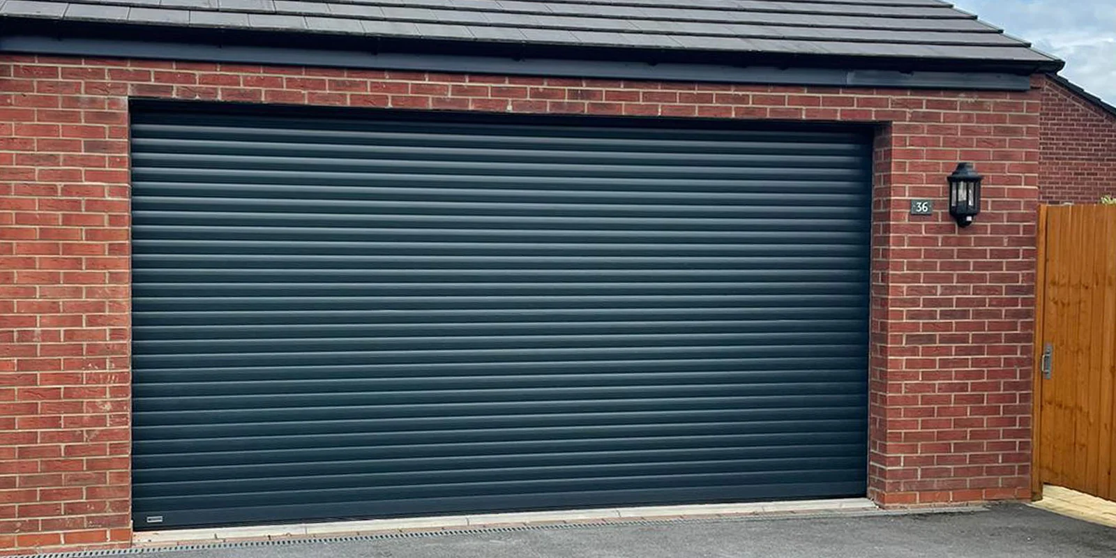 Wide anthracite roller door fitted to a red brick garage